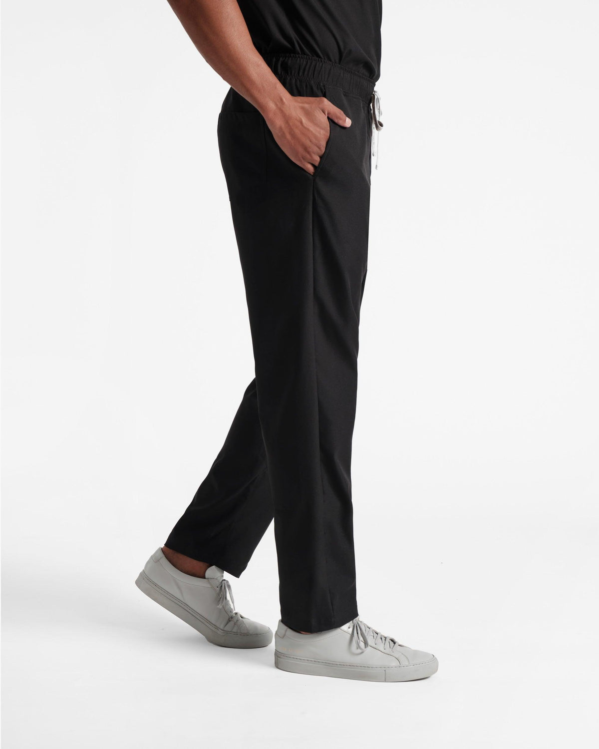 Side view of model wearing men's black straight leg scrub pants with hand in pocket.