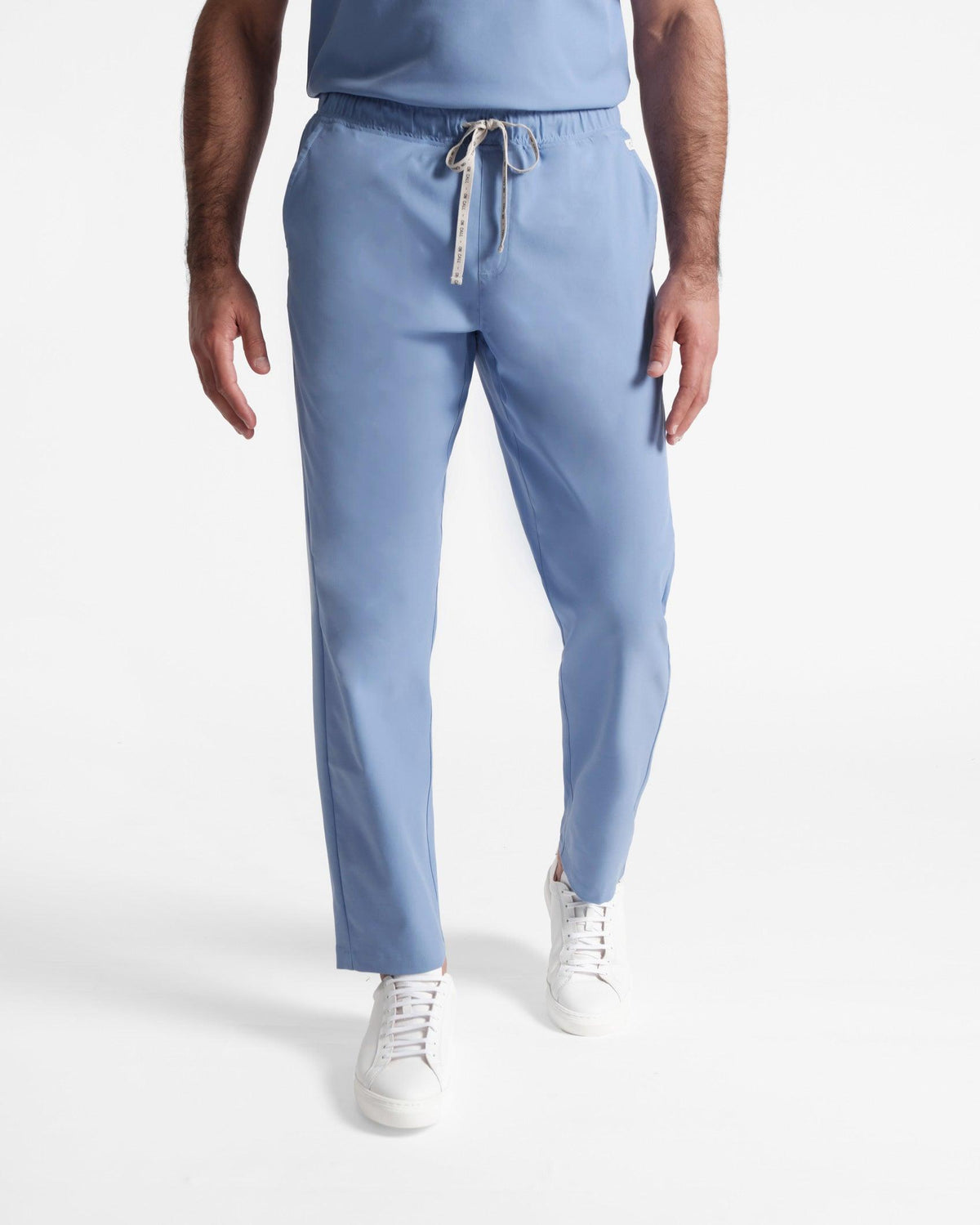 Man in light blue straight leg flat front scrub pants with a branded waistband tie.
