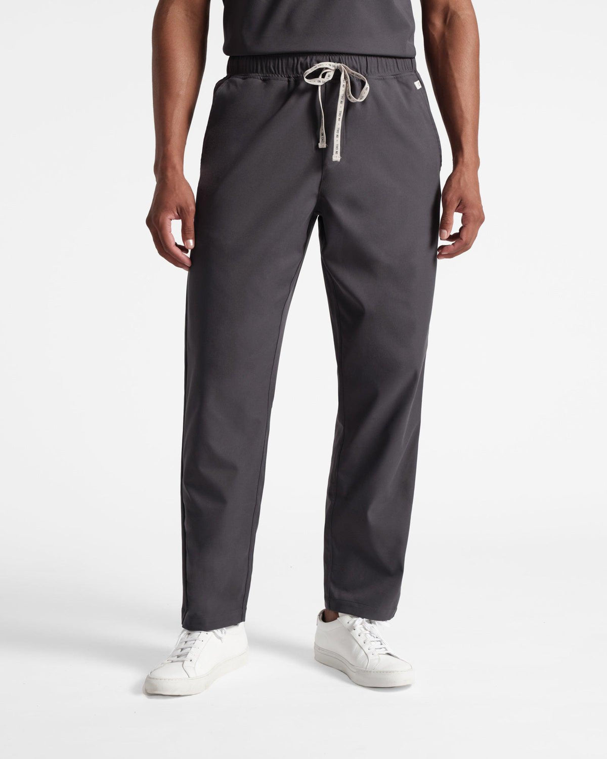 Man in dark grey straight leg scrub pants with a flat front and branded drawstring tie.