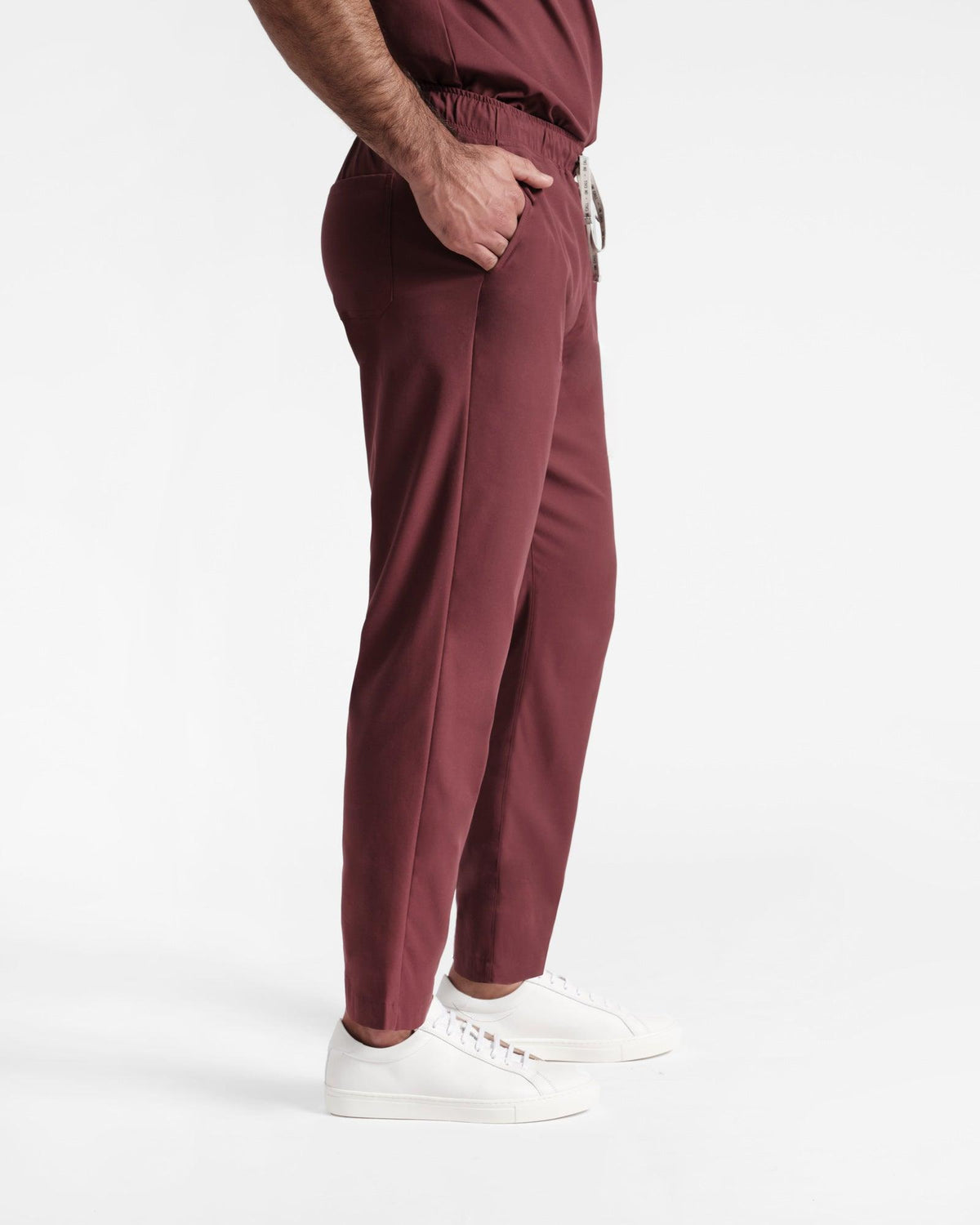 Side view of man in deep red straight leg scrub pants with hand in pocket. 
