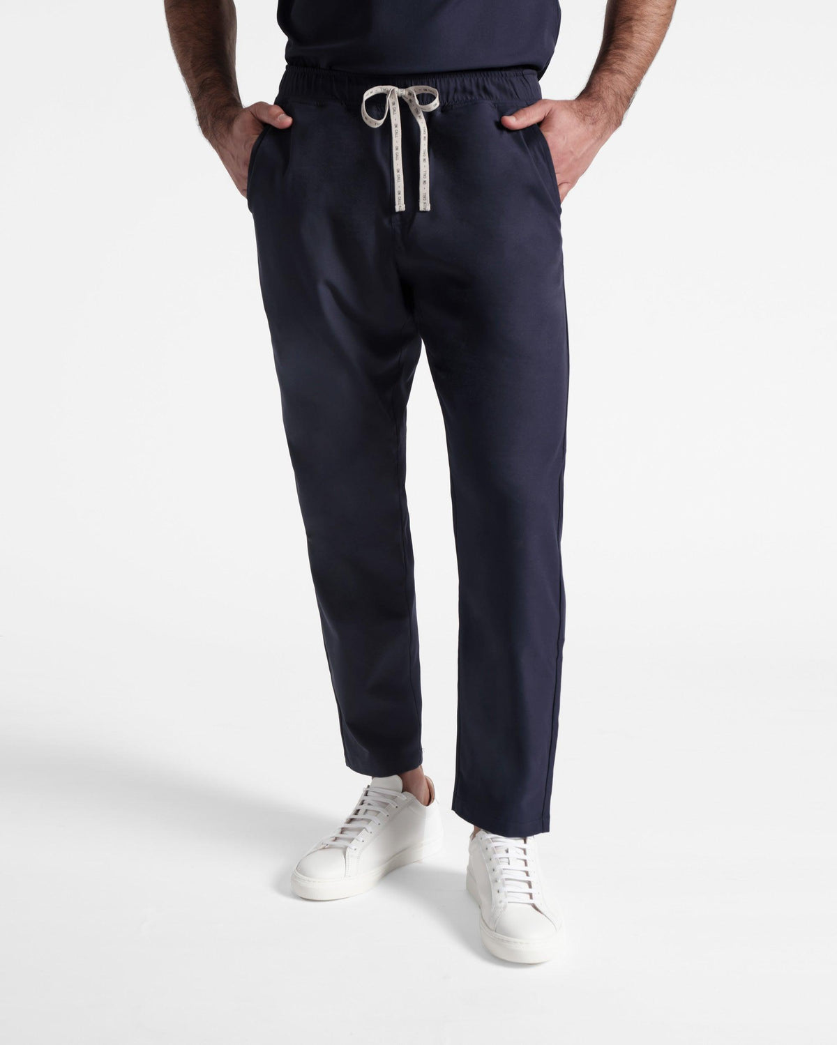 Man in navy flat front straight leg scrub pants with hands in pockets. 