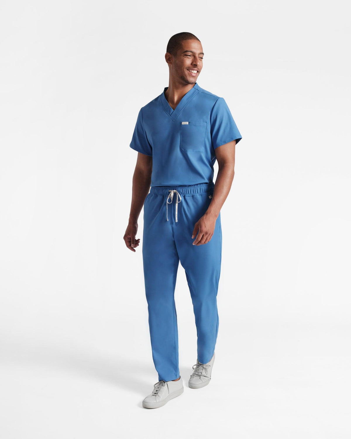 Man in bright blue straight leg scrub pants with a matching v-neck scrub shirt tucked in.
