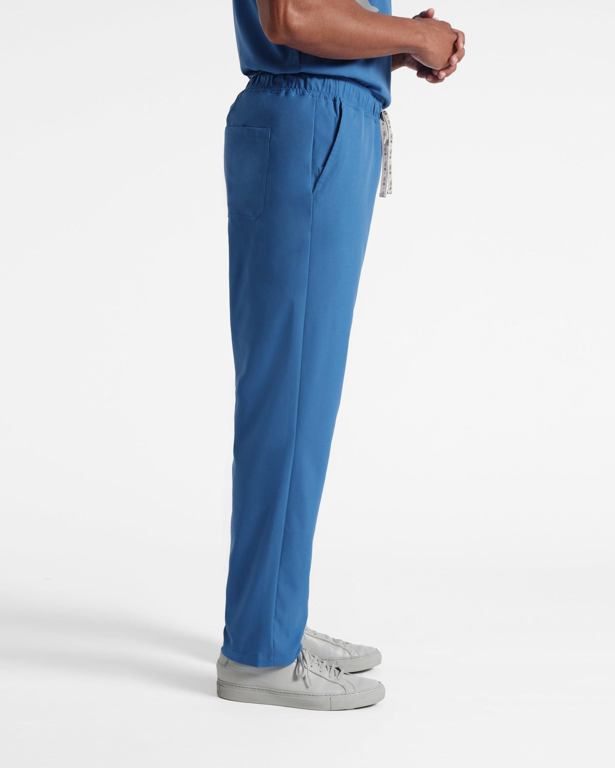 Side view of man in bright blue straight leg scrub pants with a branded drawstring. 