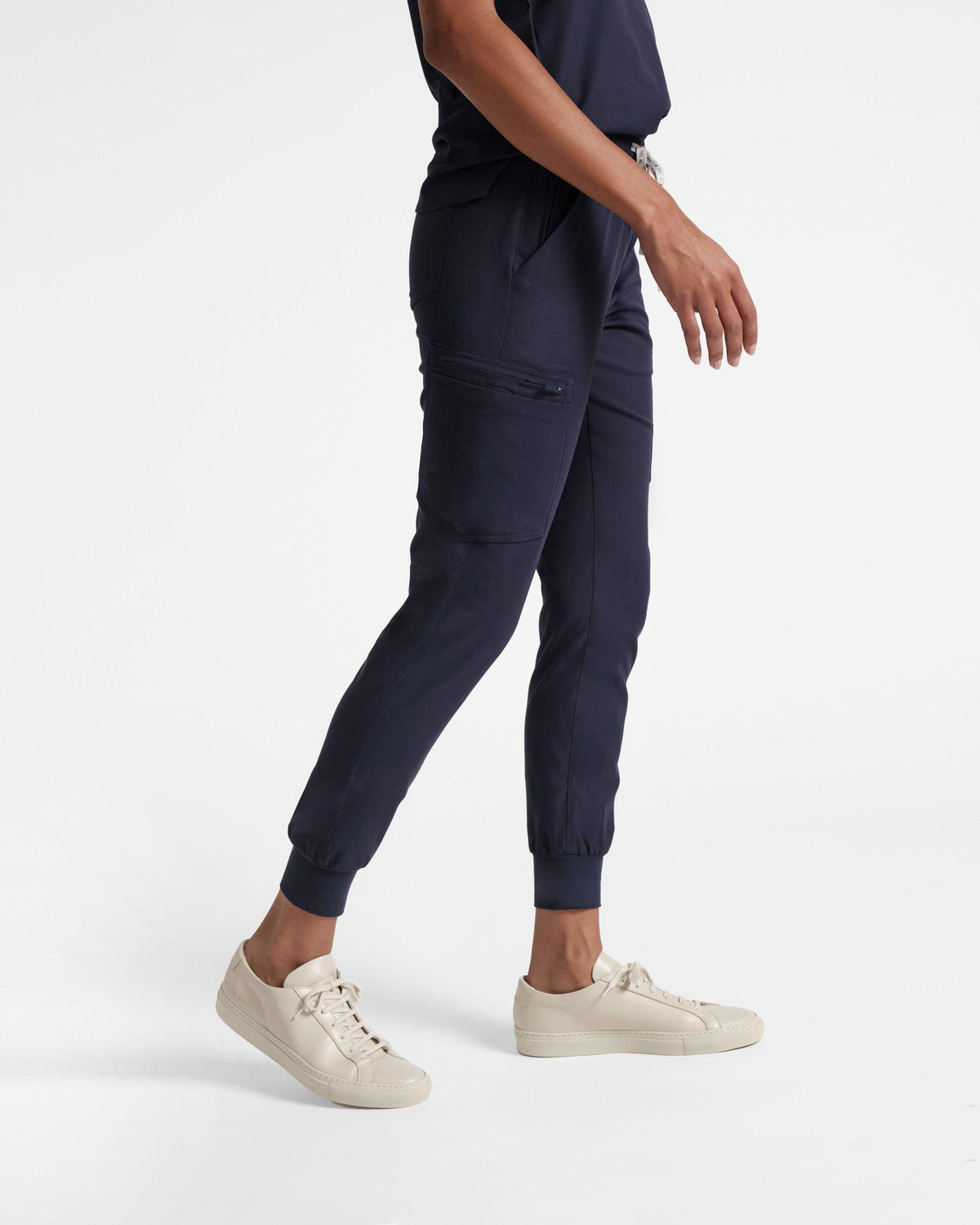 Side view of woman in cargo jogger navy scrub pants with soft ribbed ankle cuffs.