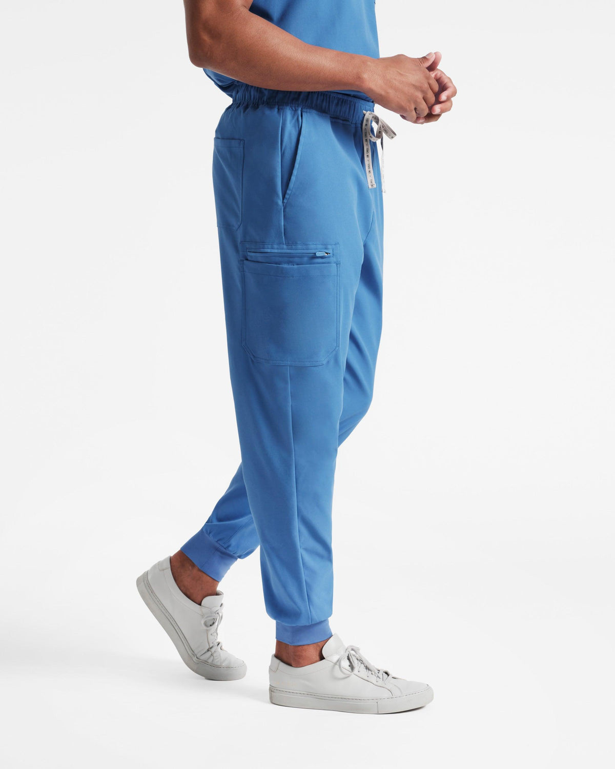 Side view of man in bright blue cargo jogger scrub pants with a large side leg pocket and branded drawstring at the waist.