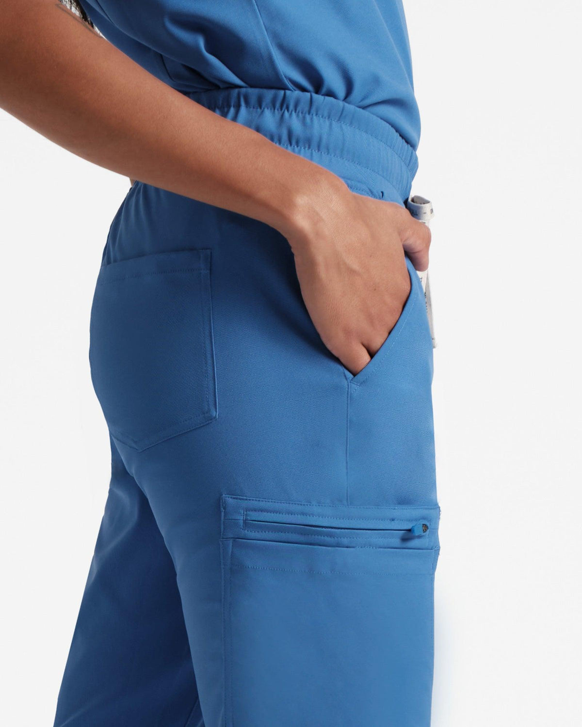 Close up side view of woman in bright blue cargo scrub pants with hand in waist pocket.