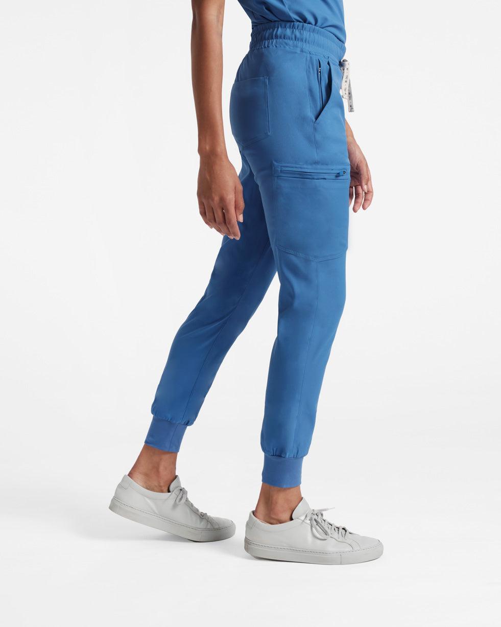 Side view of woman in bright blue jogger cargo scrub pants with a large pocket on the leg's side.