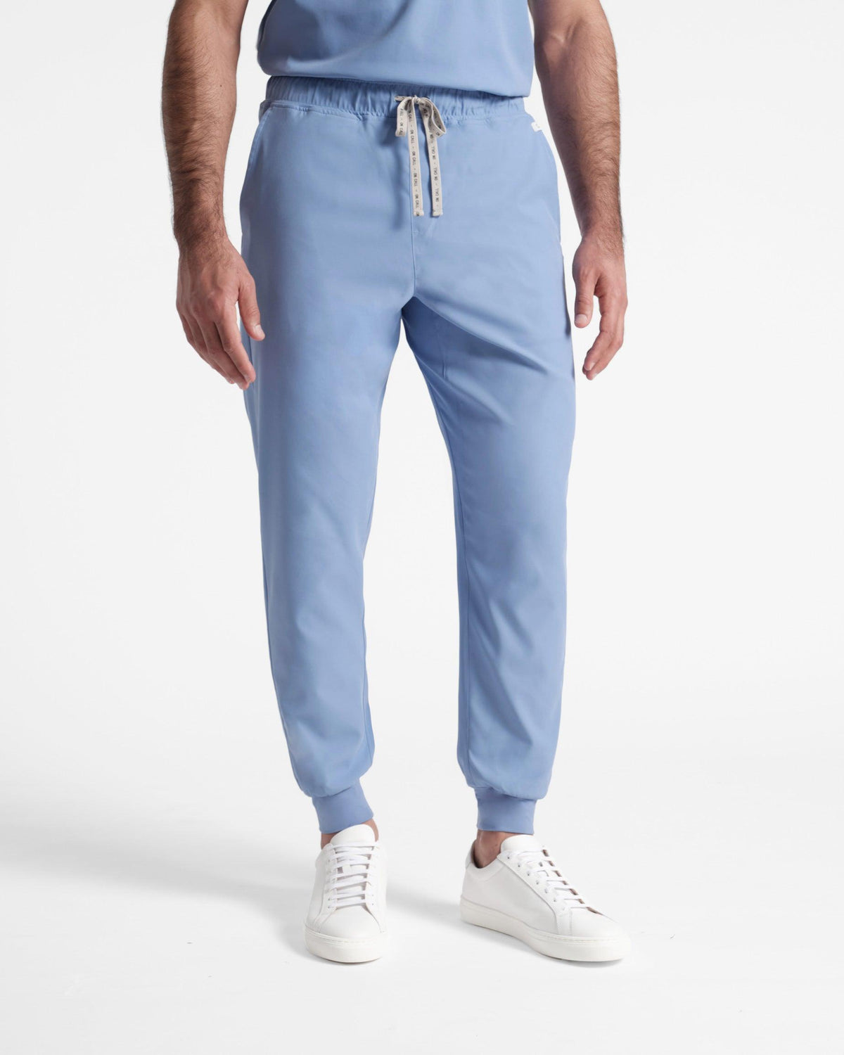 Man wearing light blue flat front jogger scrub pants with his arms resting at his sides.