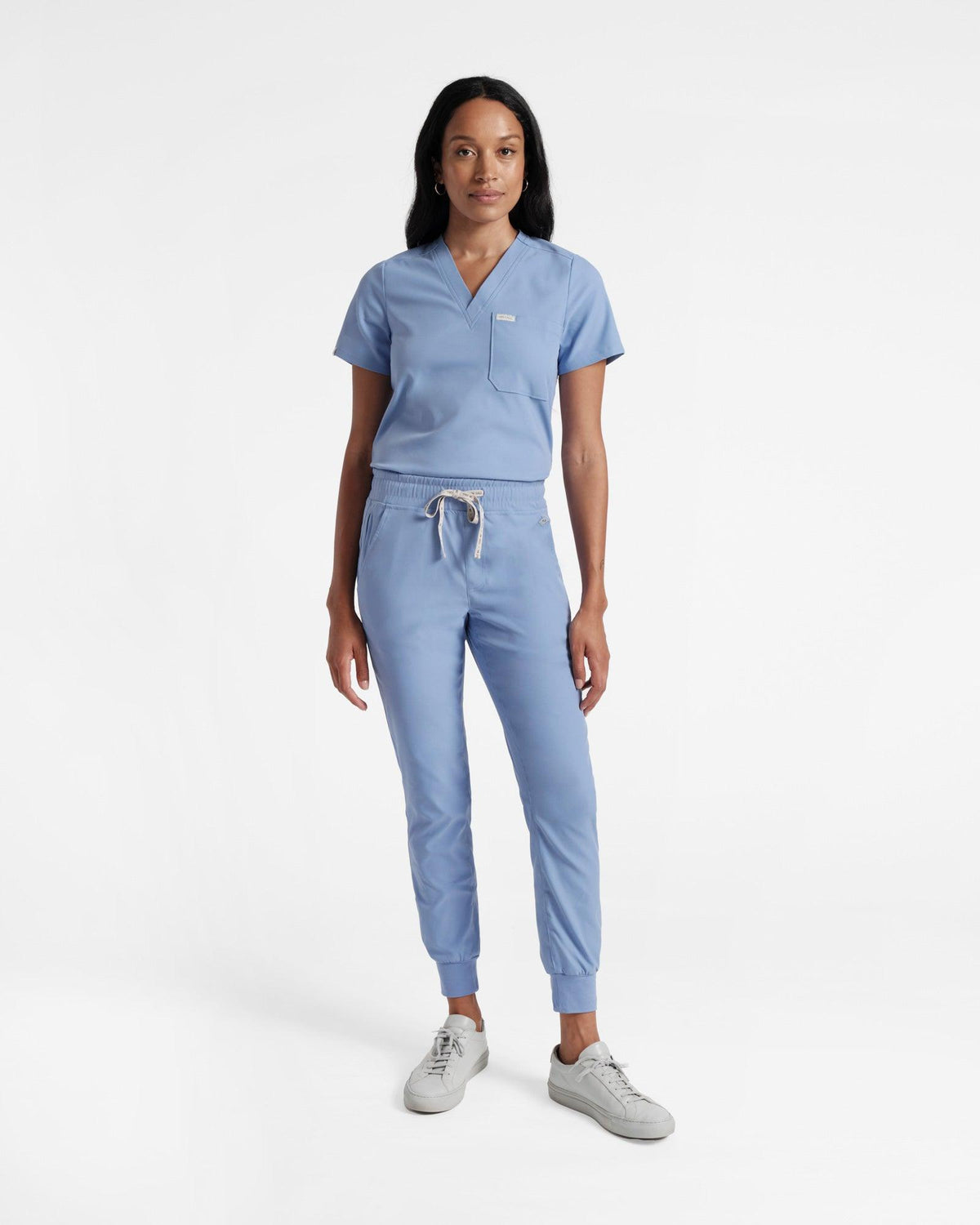 Woman in light blue jogger scrub pants and a matching v-neck top tucked in. 