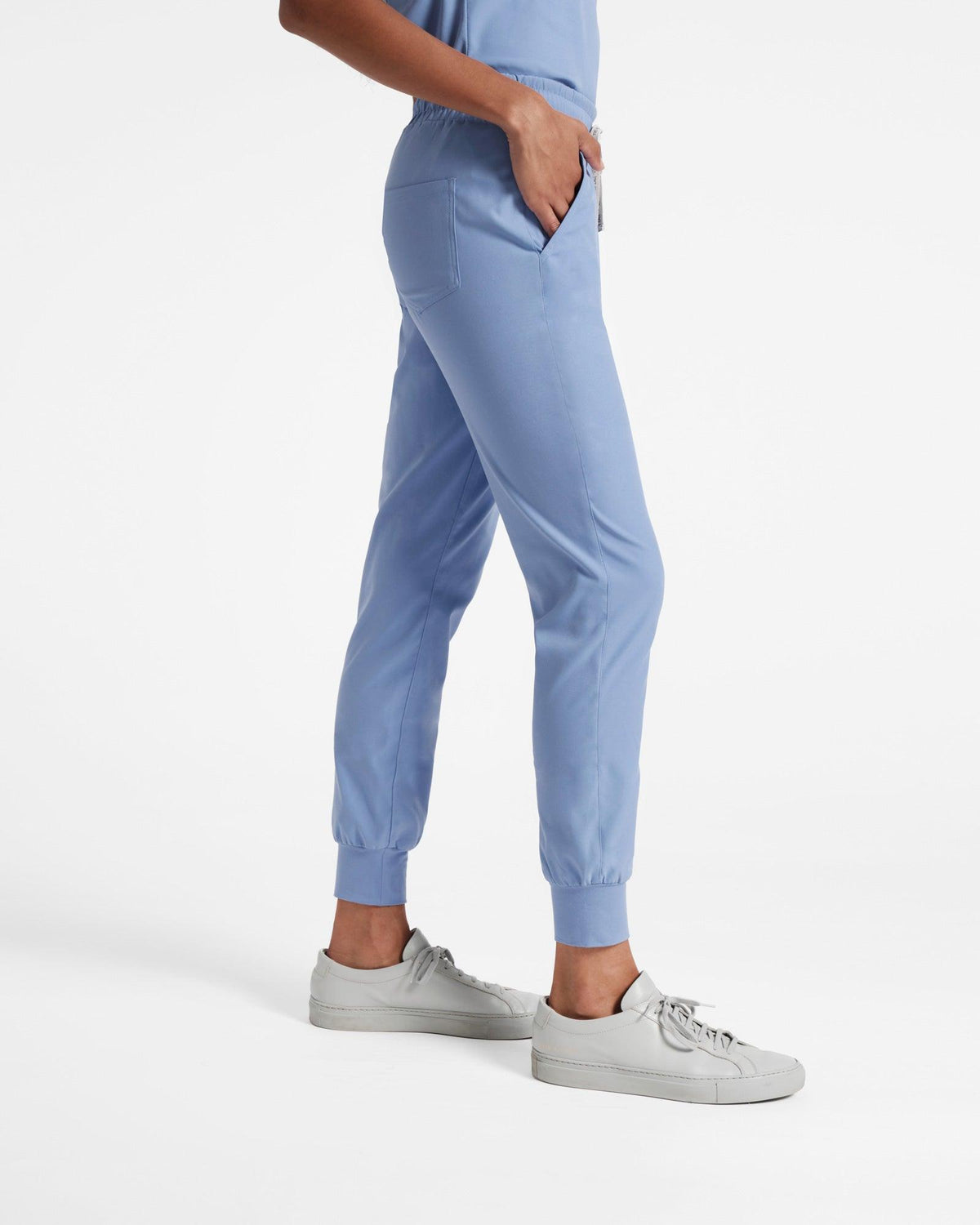 Side view of woman in light blue jogger scrub pants with her hand in the waist pocket. 