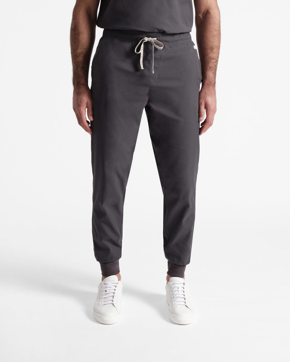 Man wearing dark grey jogger scrub pants with soft ribbed ankle cuffs.