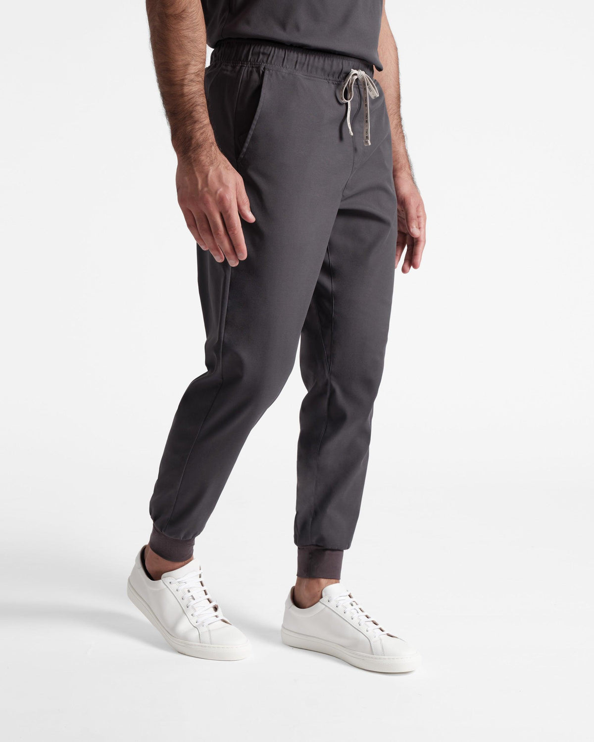 Angled side view of man wearing dark grey jogger scrub pants with a branded drawstring.