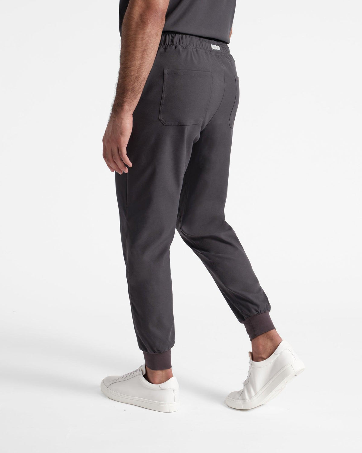 Angled back side view of man wearing dark grey jogger scrub pants with two back pockets.