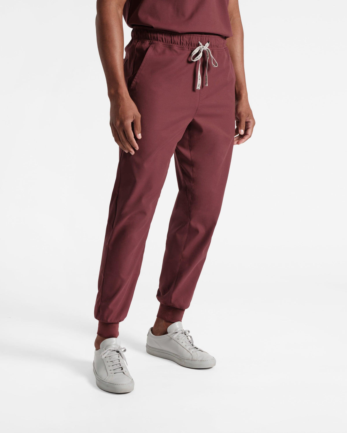 Man in deep red jogger scrub pants with a branded drawstring at the waist and soft ribbed ankle cuffs.