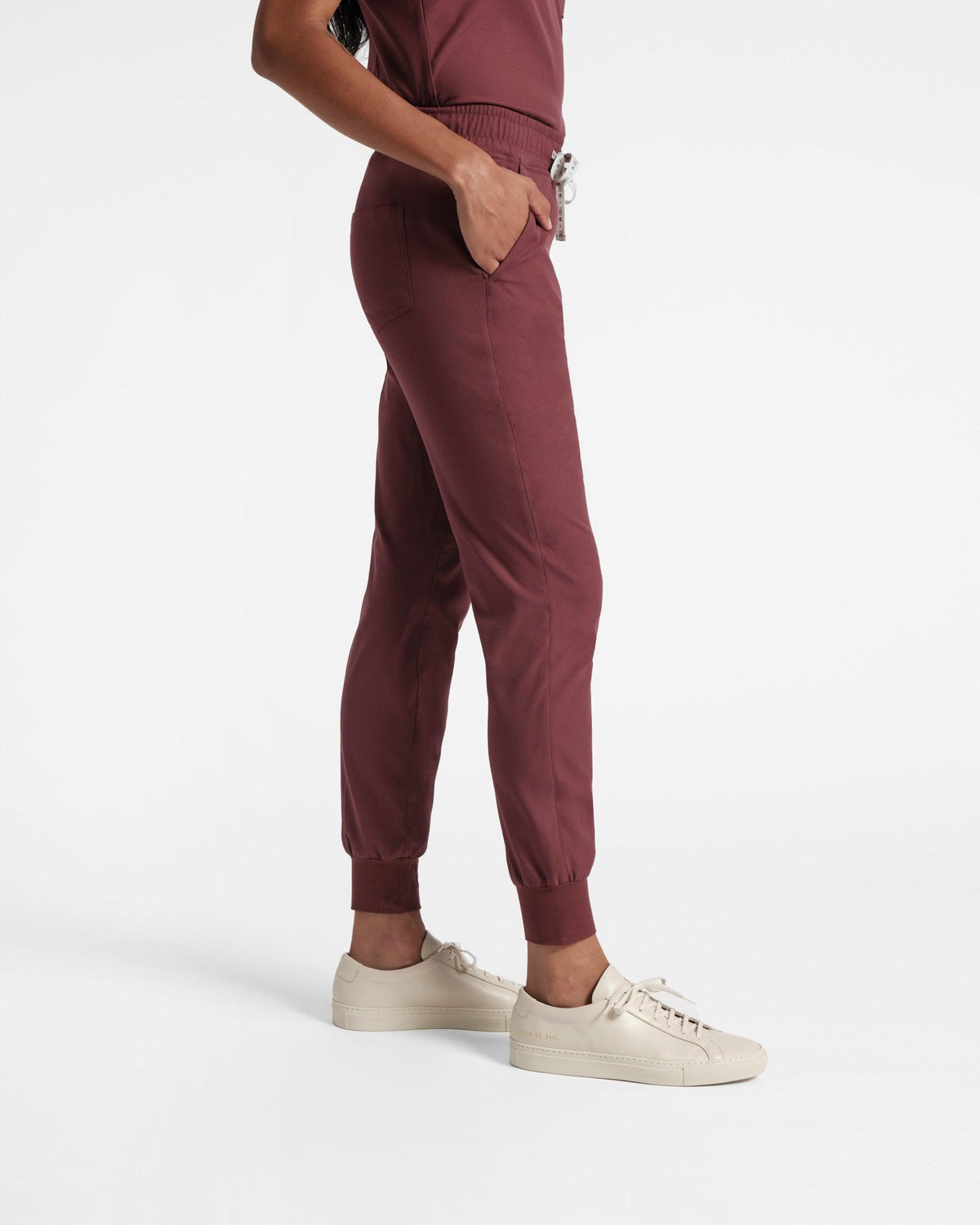 Side view of woman in deep red jogger cargo scrub pants with hand in pocket.