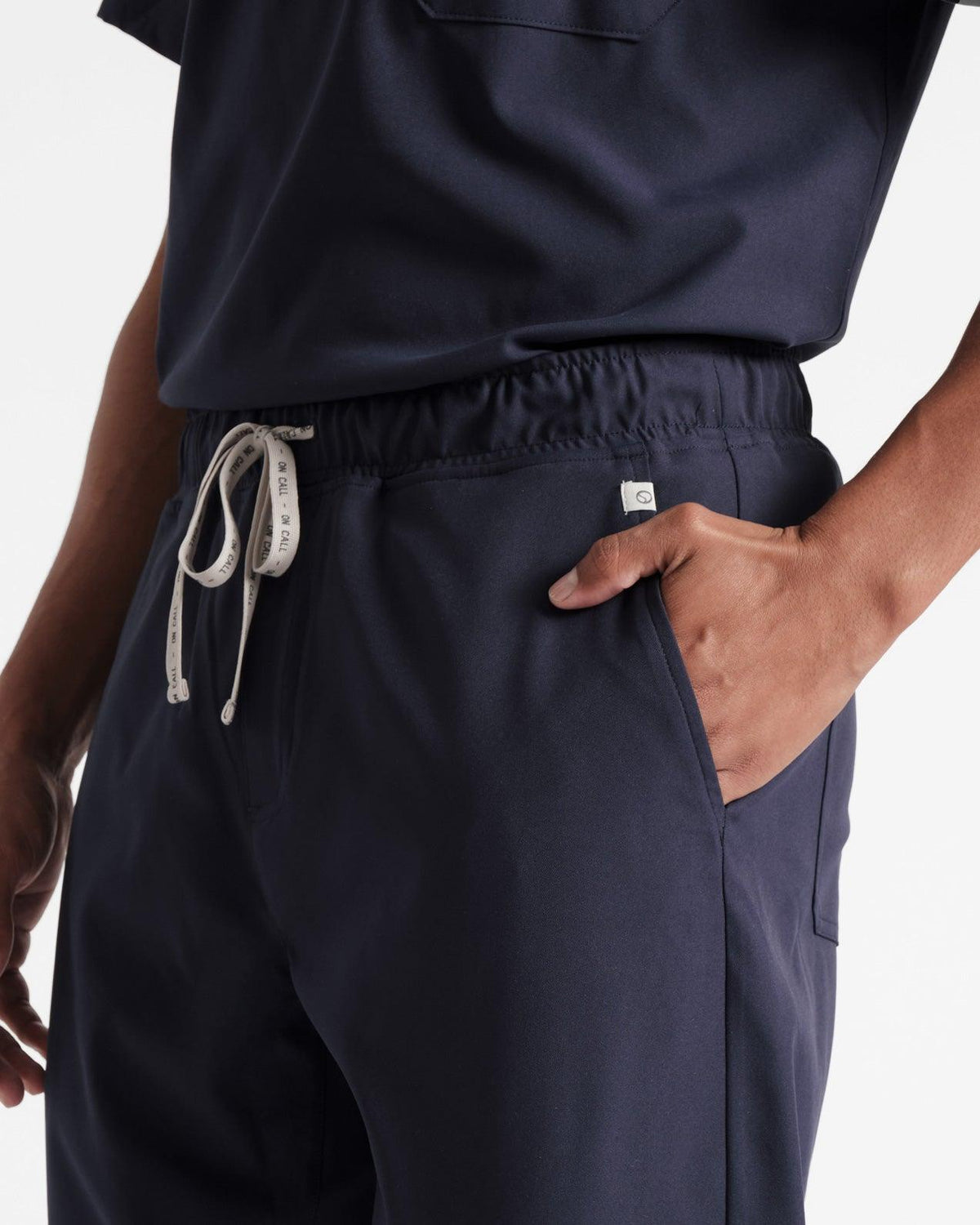 Detailed view of man wearing navy scrub pants, focused on his hand in the pocket and branded drawstring at the waist.