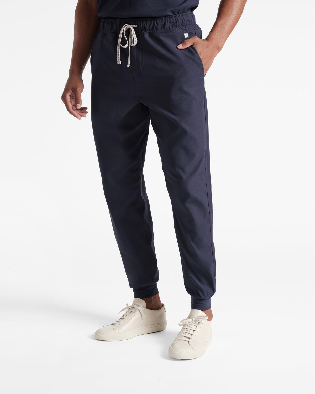 Man wearing navy jogger scrub pants with a branded drawstring and a logo fabric label wrapped around the pocket seam.