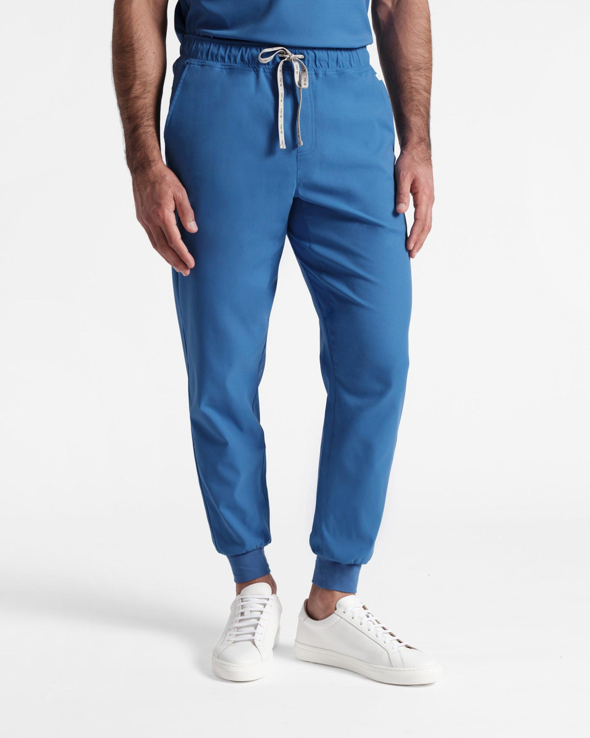 Man in bright blue jogger scrub pants with a branded drawstring and arms resting at his sides.