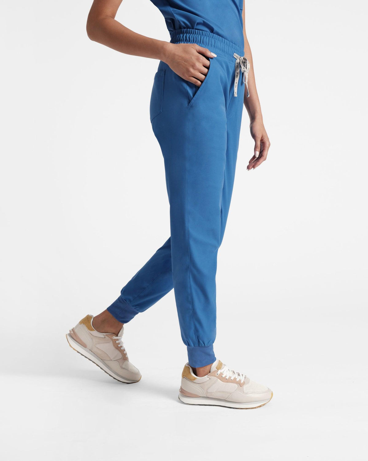 Woman in bright blue jogger scrub pants with soft ribbed ankle cuffs and hand in pocket.