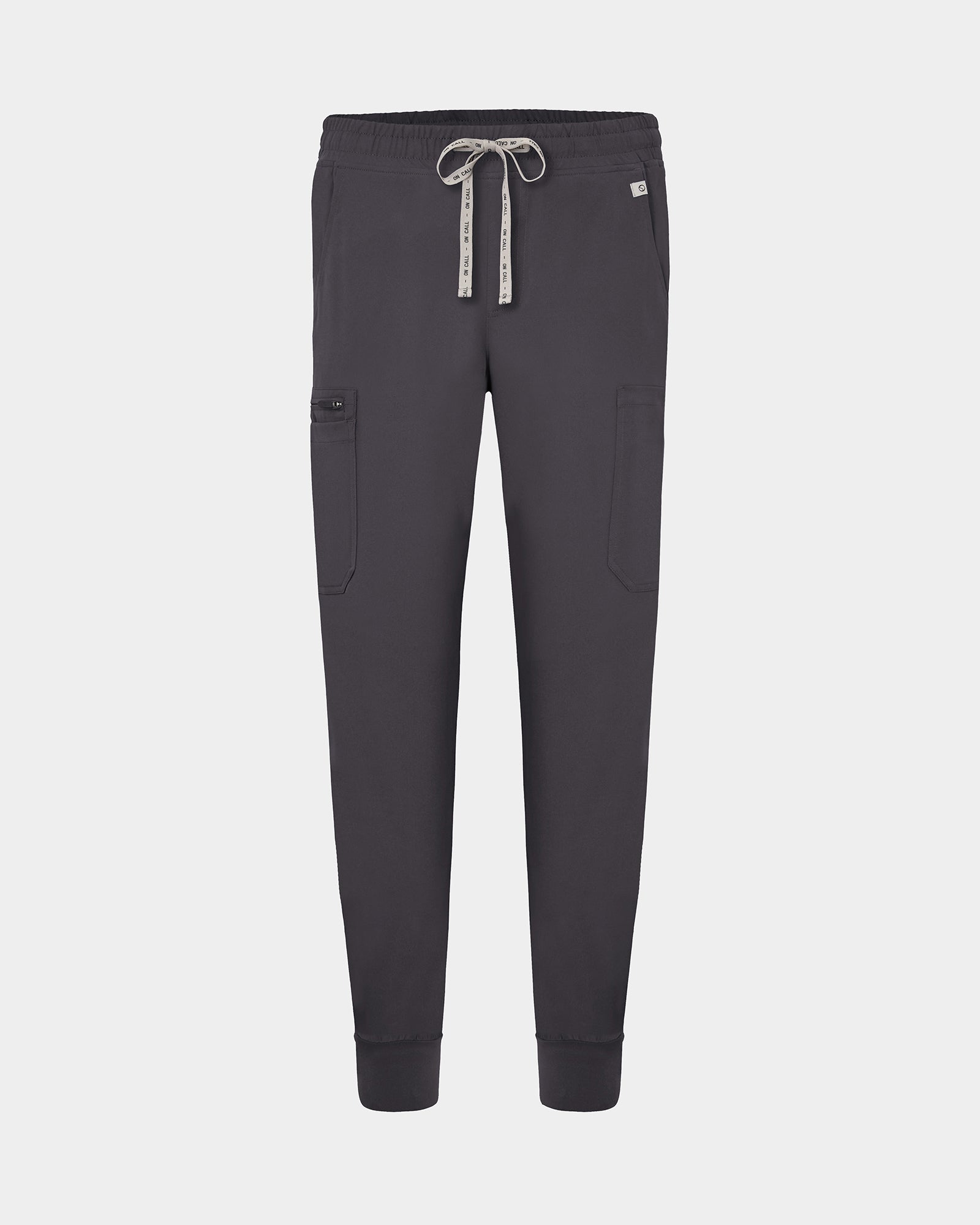 Dark grey jogger-style scrub pants with an elastic waistband, white logo drawstring, and side cargo pocket, shown on a light gray background.