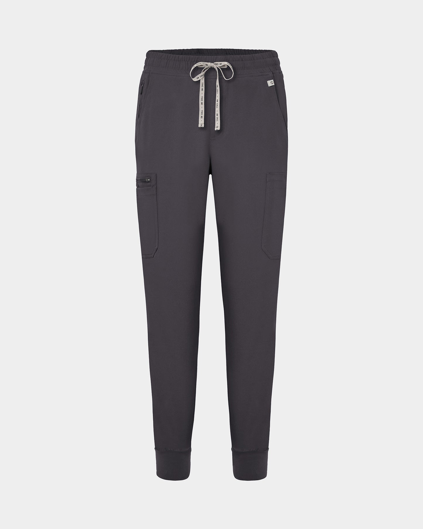 Dark grey jogger-style scrub pants with a white drawstring, cargo pockets, and a small white logo on the upper right hip, shown against a light gray background.