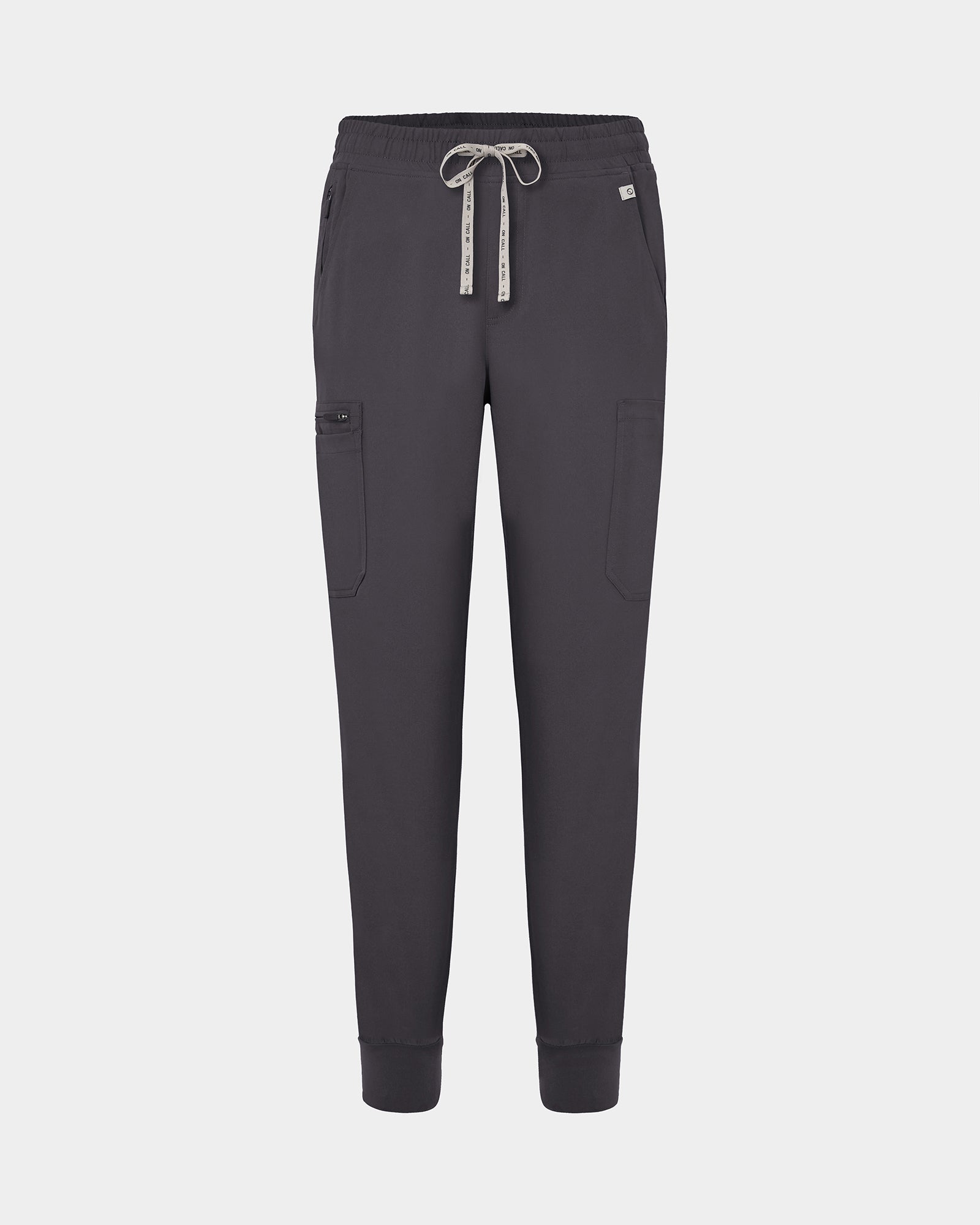Dark grey jogger-style scrub pants with a white drawstring, cargo pockets, and a small white logo on the upper right hip, shown against a light gray background.
