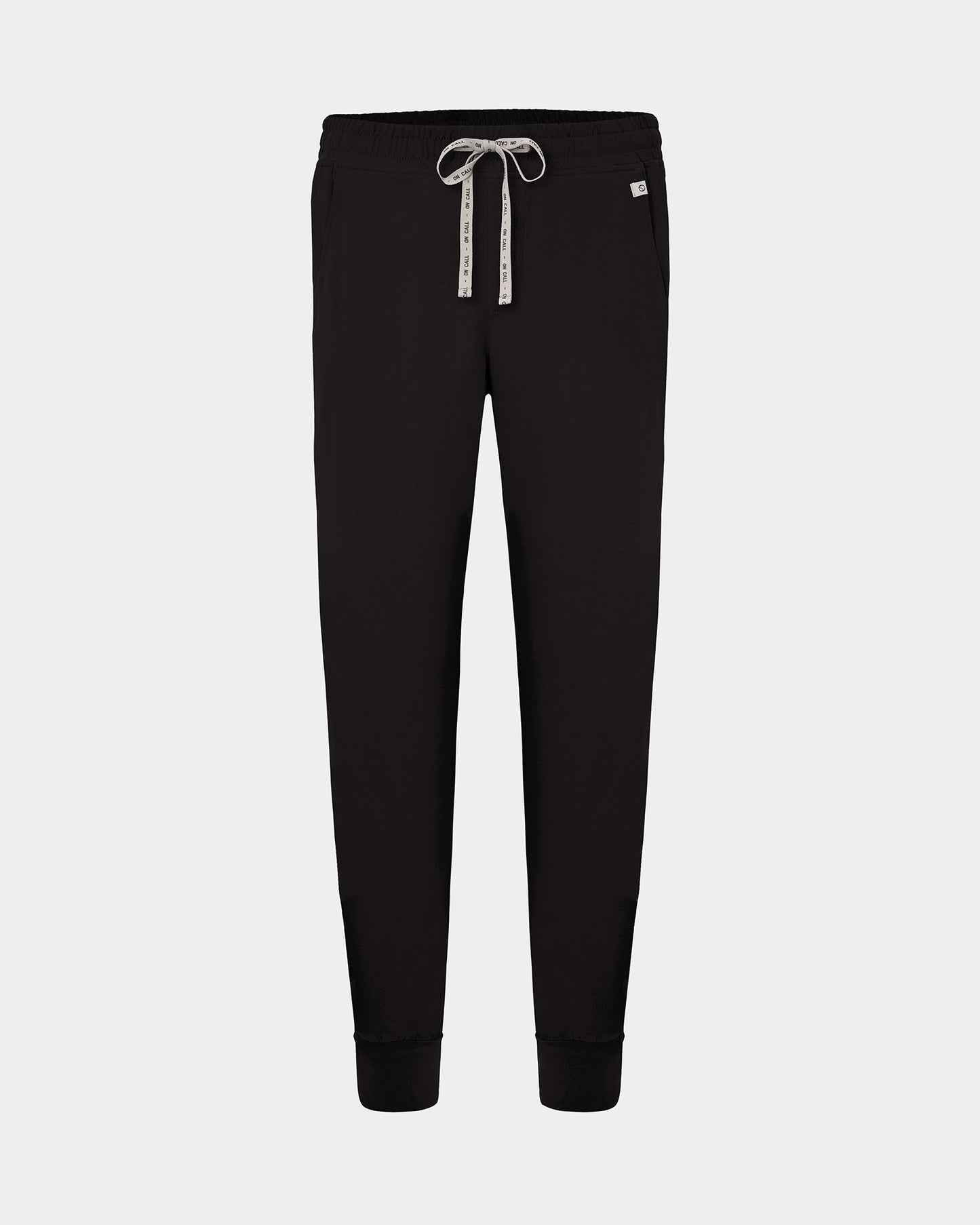Black jogger scrub pants with a white patterned drawstring and a small white brand tag on the right hip, shown against a light gray background.