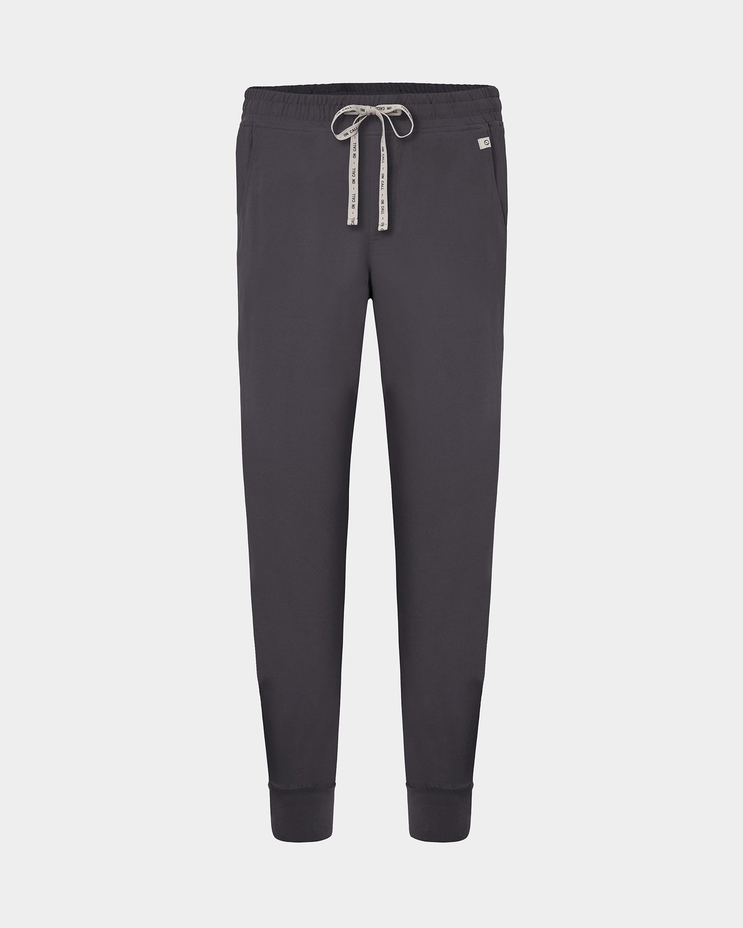 Dark gray jogger scrub pants with an elastic waistband, white patterned drawstring, and ribbed cuffs, shown against a light gray background.
