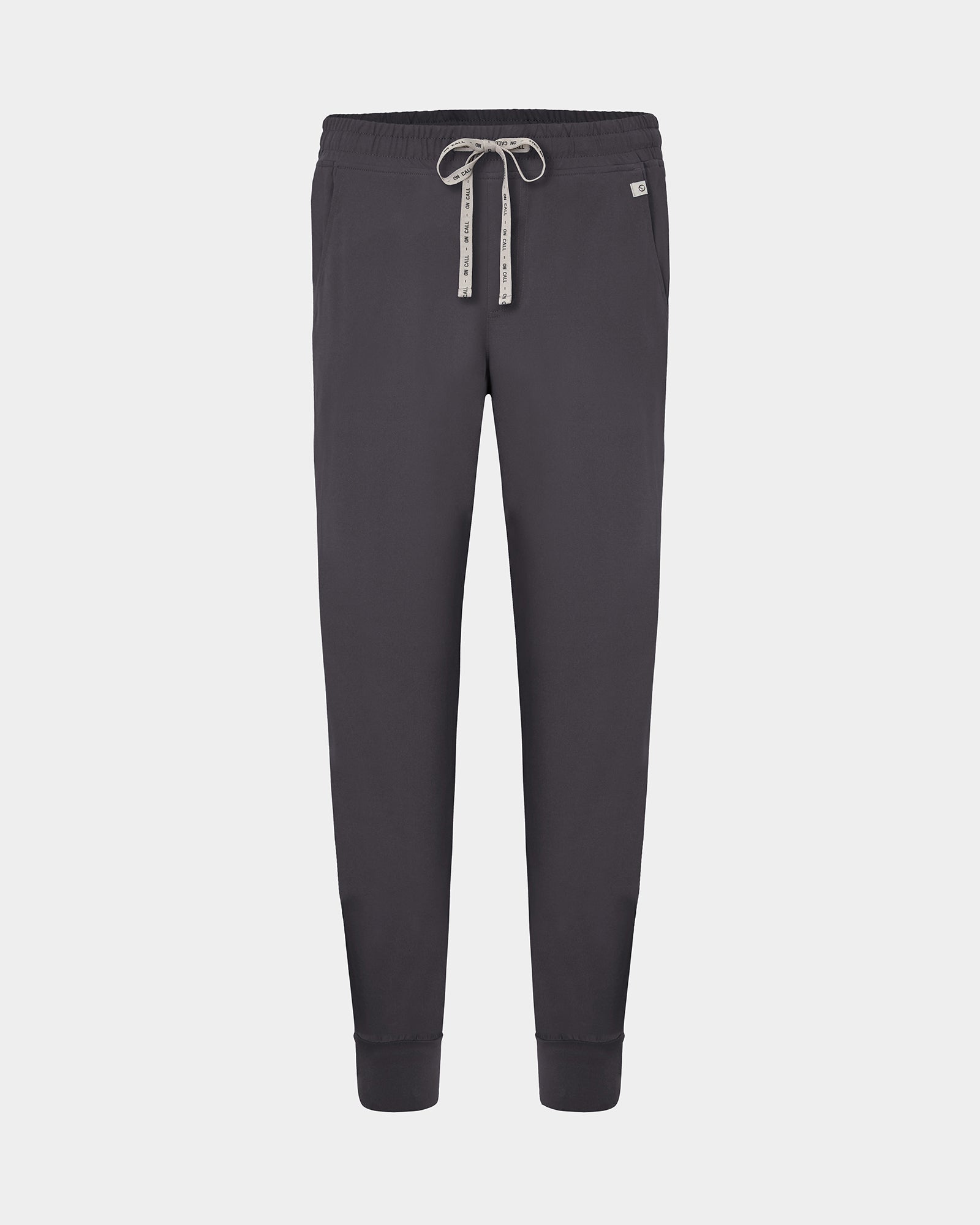 Dark gray jogger scrub pants with an elastic waistband, white patterned drawstring, and ribbed cuffs, shown against a light gray background.