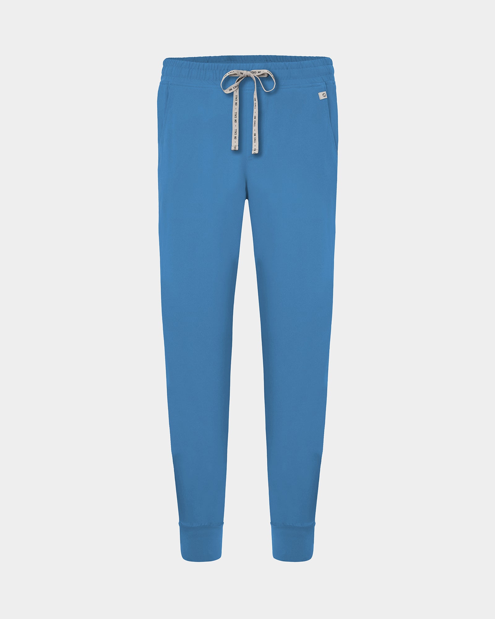 Bright blue jogger-style scrub pants with an elastic waistband, logo drawstring, and ankle cuffs, shown on a light gray background.