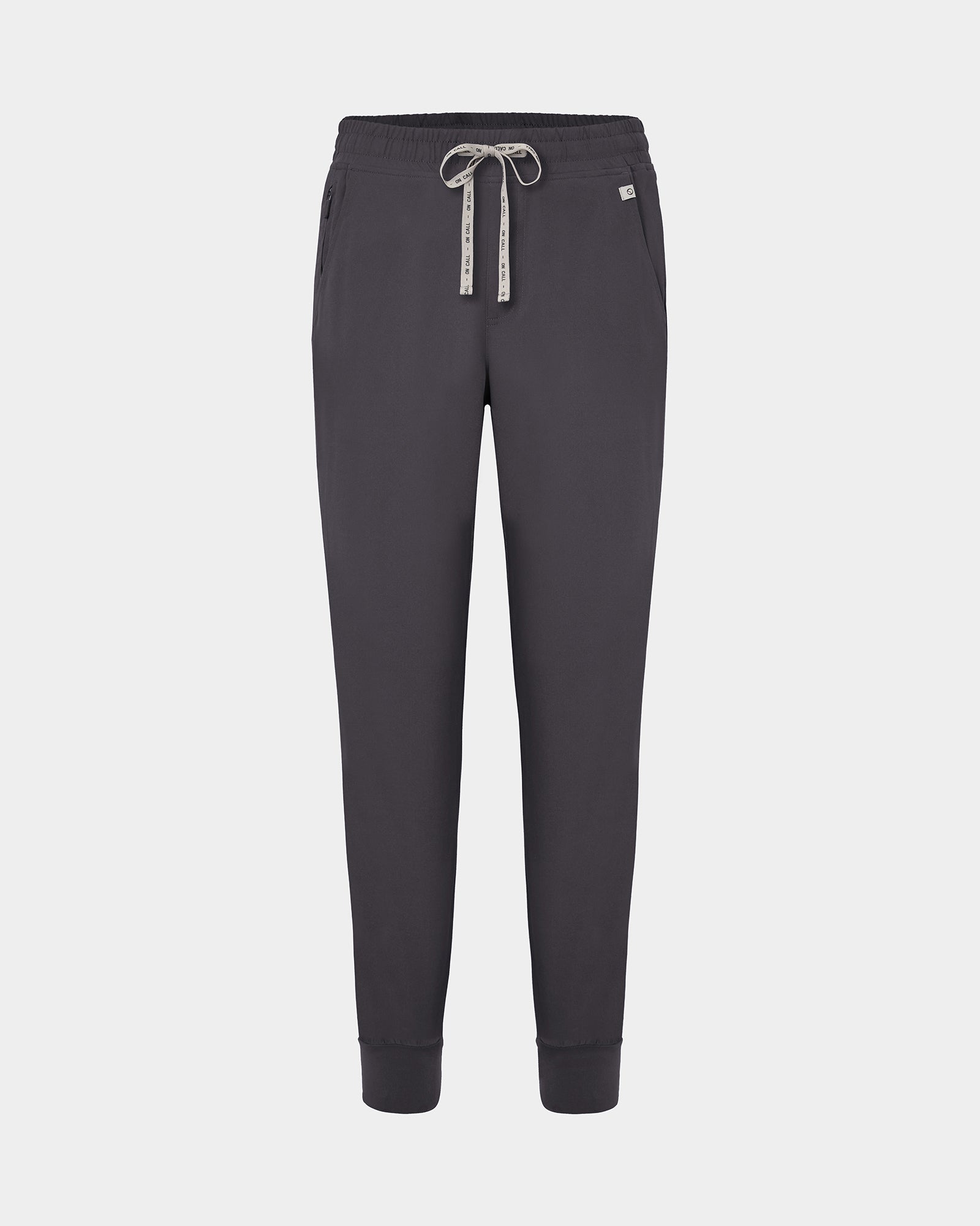 Dark grey jogger scrub pants with a logo drawstring, ankle cuffs, and a small white logo on the left hip, shown against a light gray background.