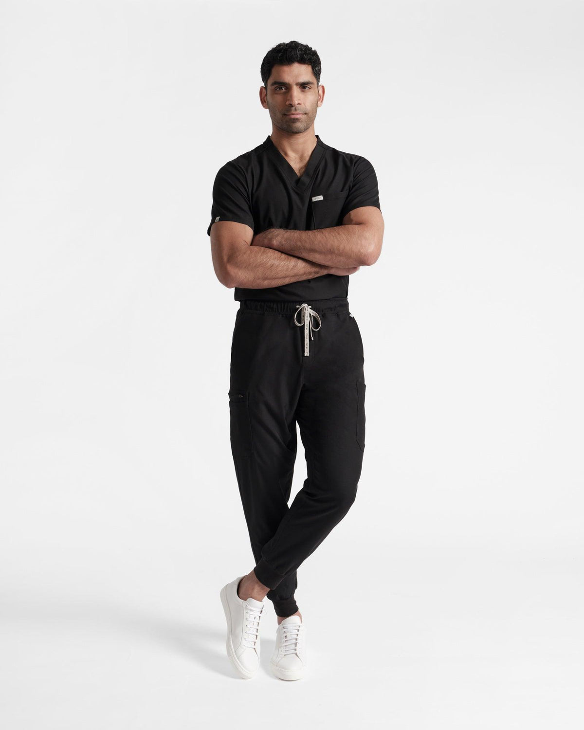 Model wearing men's black cargo jogger scrub pants and a matching shirt with arms crossed.