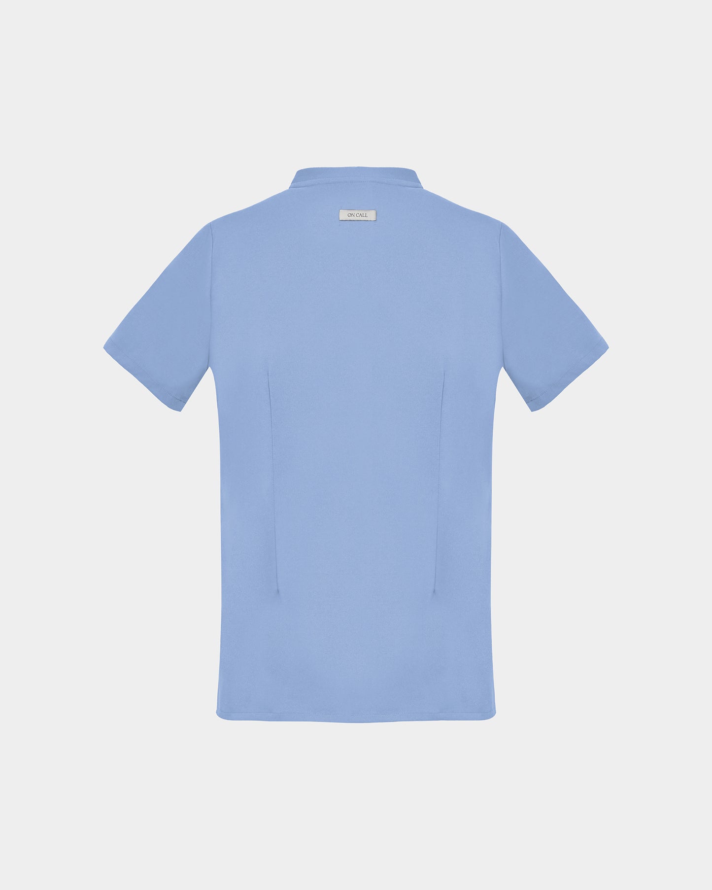 A light blue short-sleeve scrub shirt shown from the back, featuring two darts, centered on a light gray background.