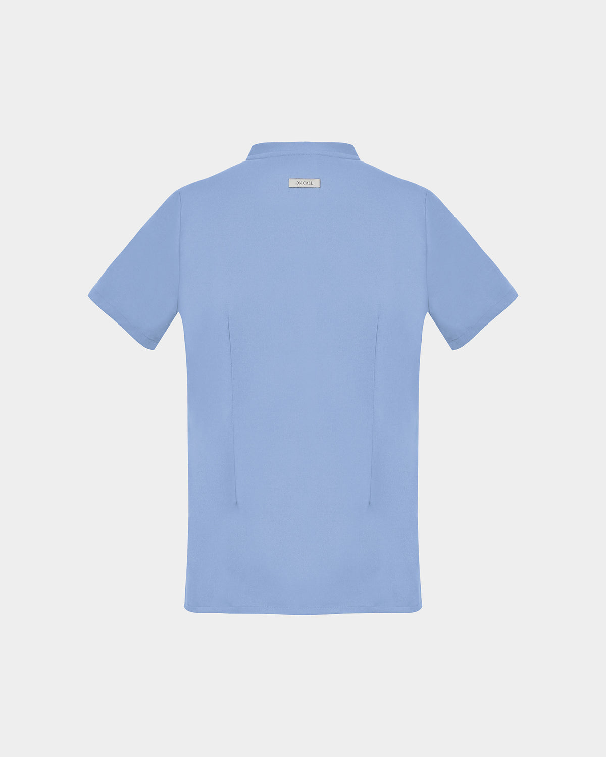 A light blue short-sleeve scrub shirt shown from the back, featuring two darts, centered on a light gray background.