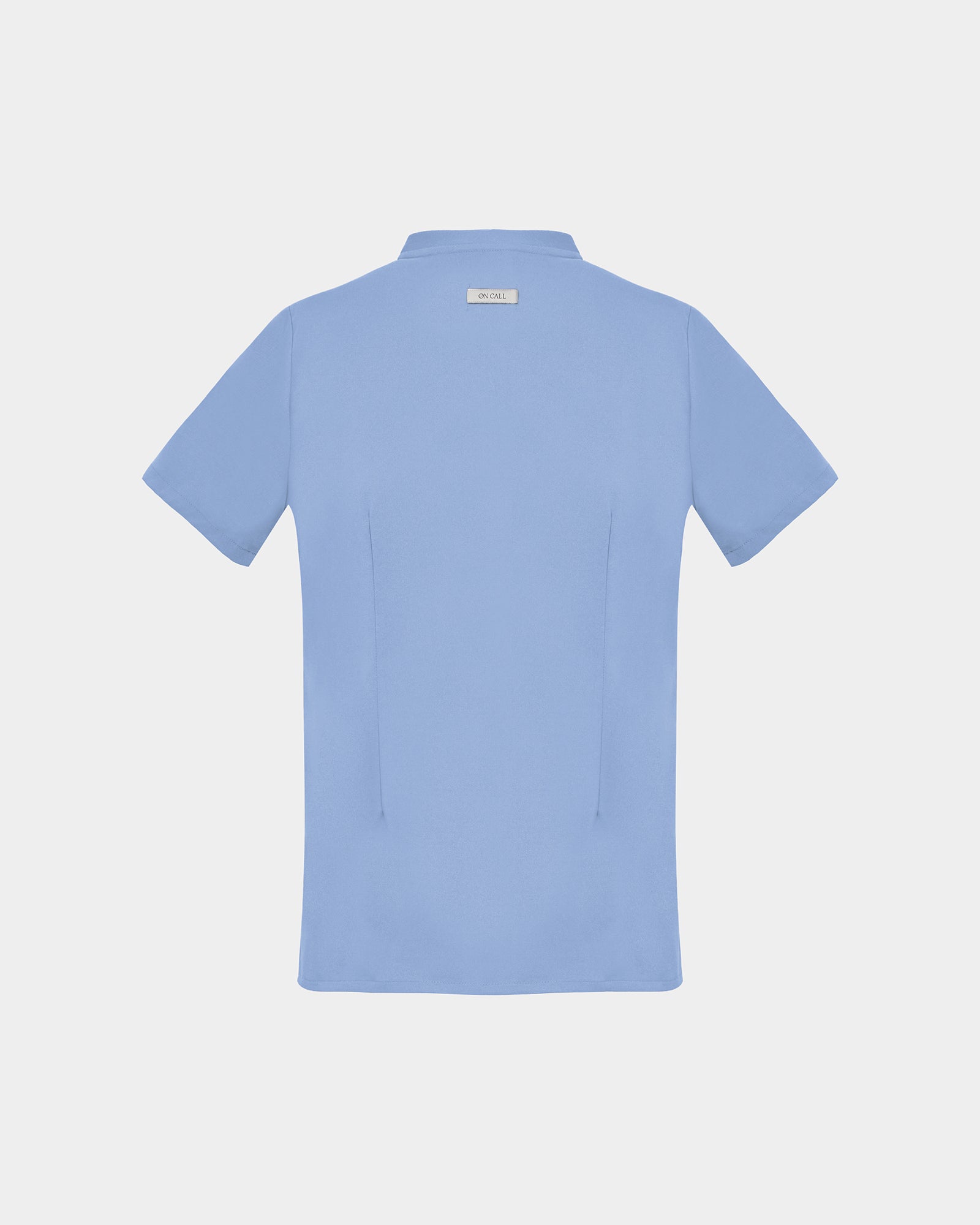 A light blue short-sleeve scrub shirt shown from the back, featuring two darts, centered on a light gray background.