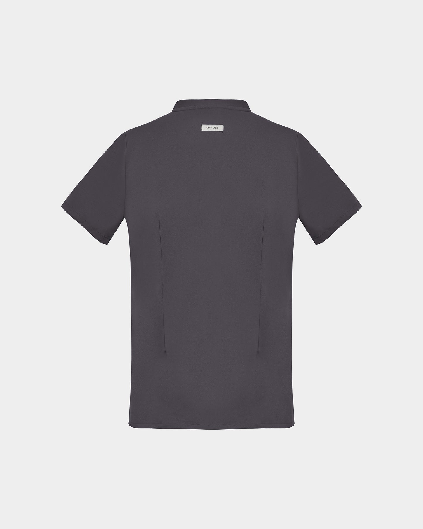 A dark gray short-sleeve scrub shirt shown from the back, featuring two subtle darts and a small rectangular brand label at the collar, set against a solid light gray background.