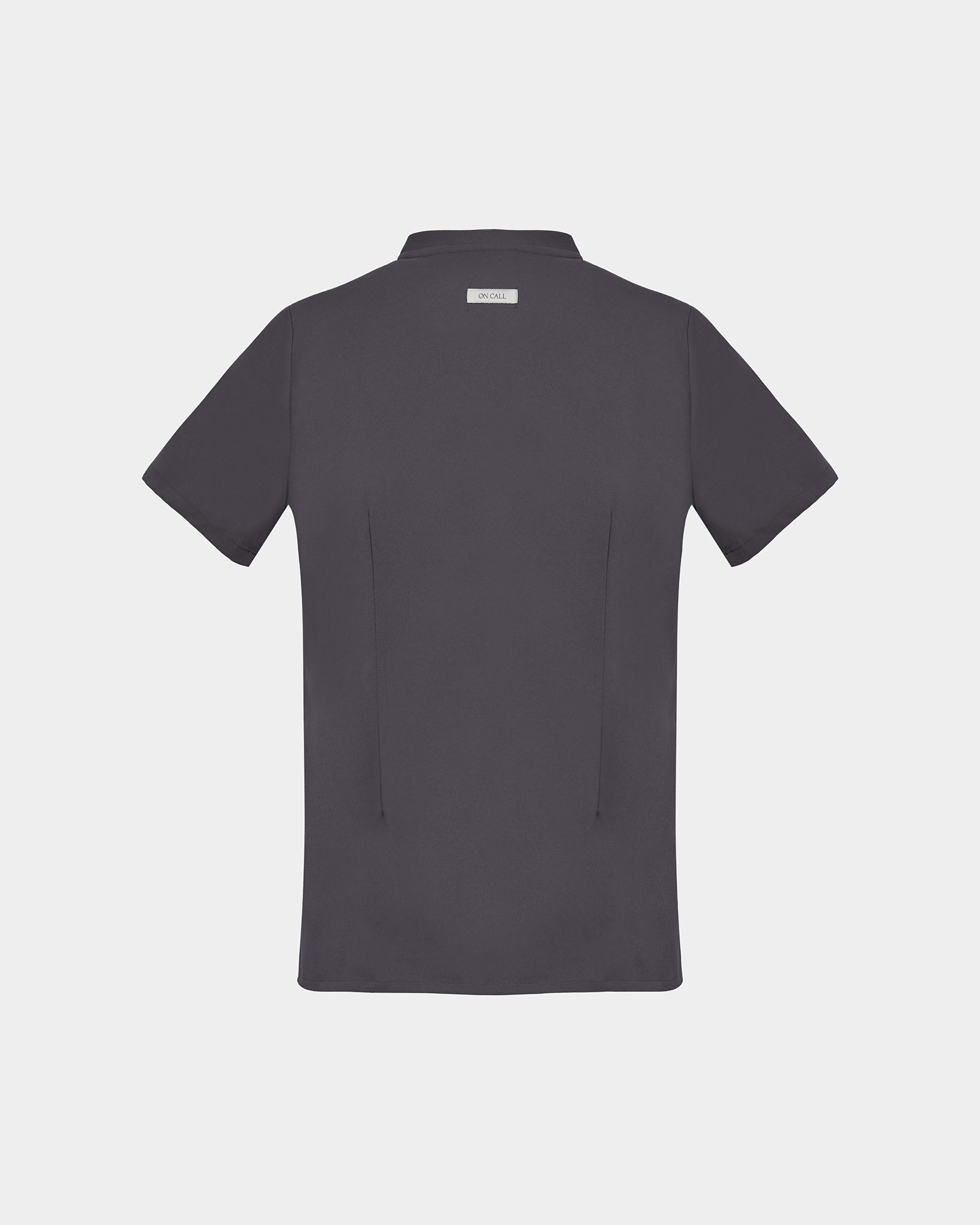 A dark gray short-sleeve scrub shirt shown from the back, featuring two subtle darts and a small rectangular brand label at the collar, set against a solid light gray background.