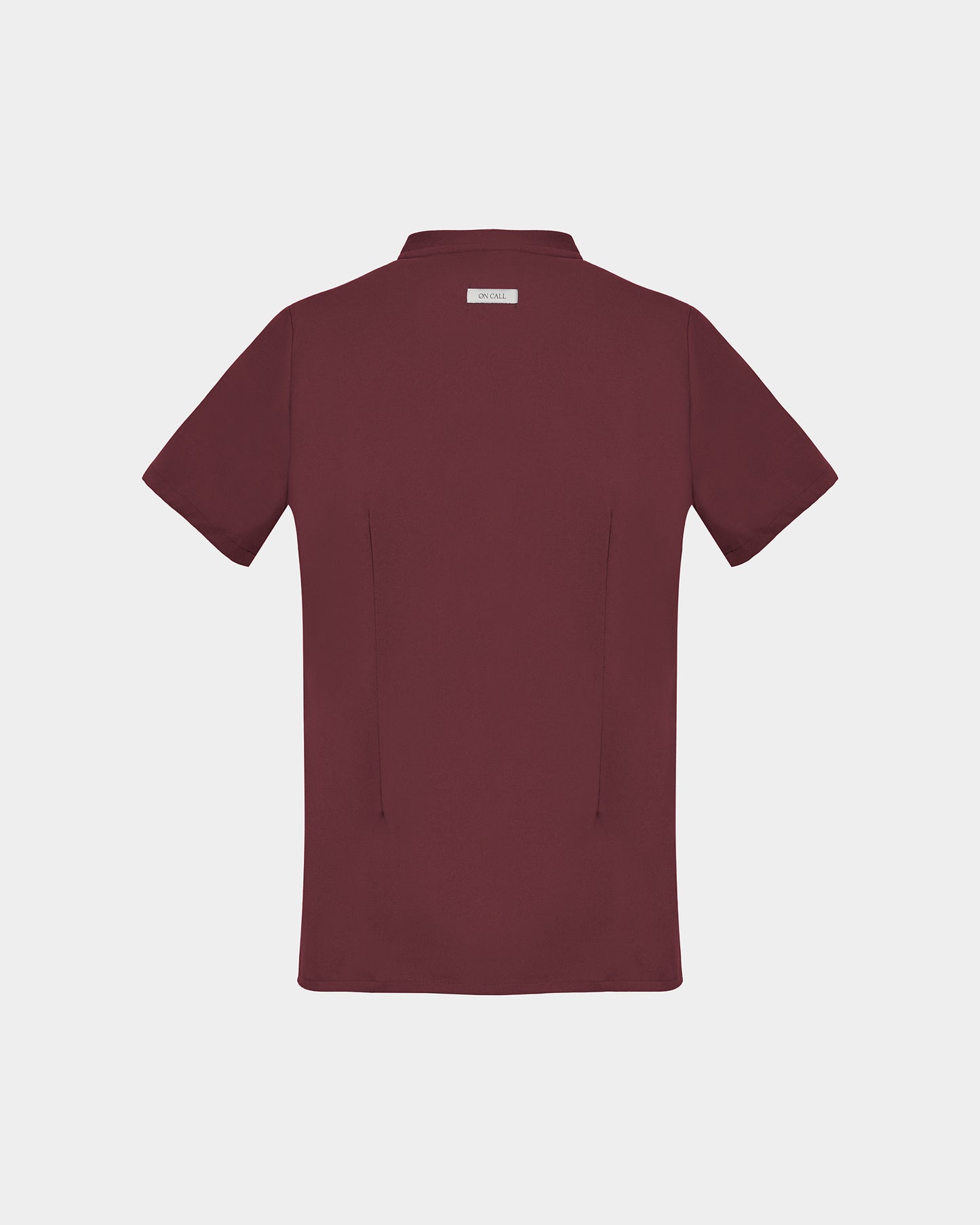 A short-sleeve scrub shirt in a deep heme red color, shown from the back, featuring two subtle darts, against a light gray background.