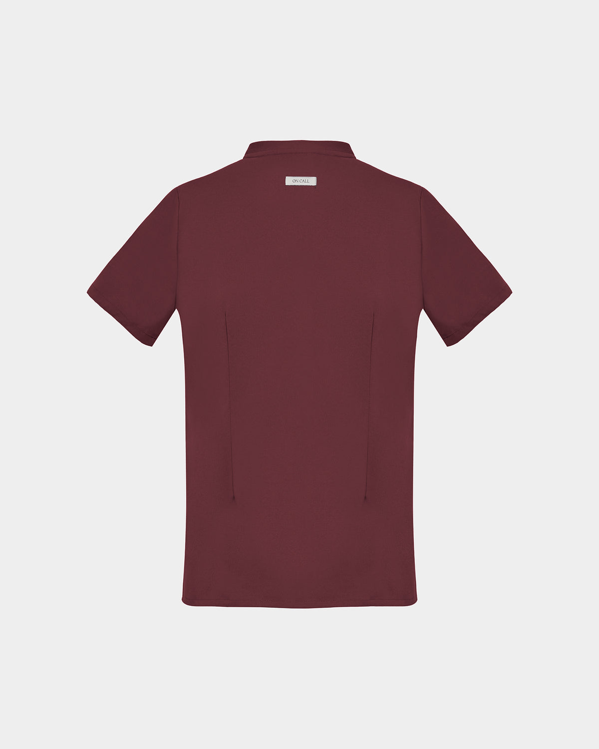 A short-sleeve scrub shirt in a deep heme red color, shown from the back, featuring two subtle darts, against a light gray background.
