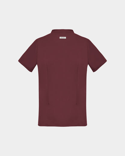 A short-sleeve scrub shirt in a deep heme red color, shown from the back, featuring two subtle darts, against a light gray background.