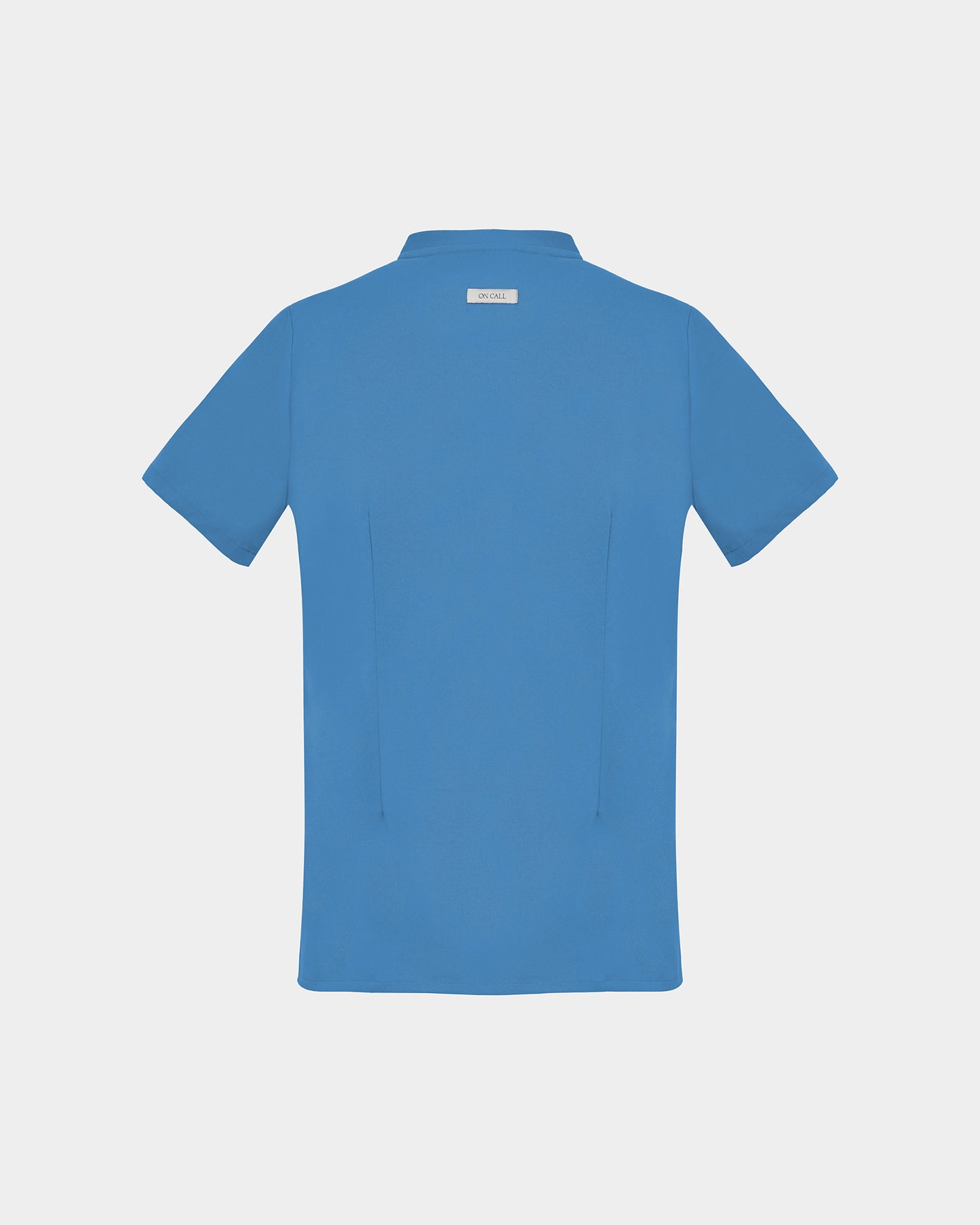 A short-sleeve scrub shirt in a solid bright blue color, featuring two subtle darts, shown from the back against a light gray background.