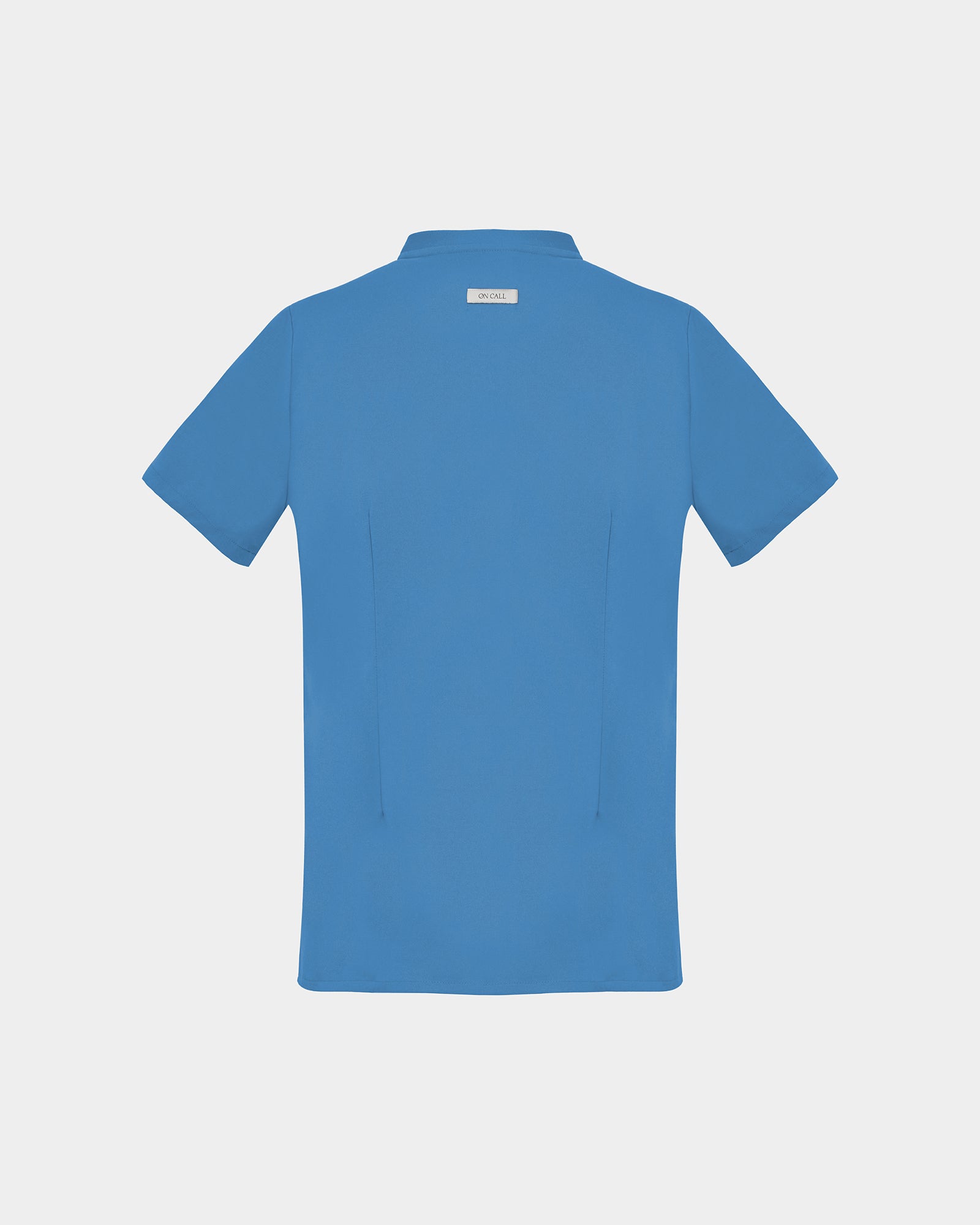 A short-sleeve scrub shirt in a solid bright blue color, featuring two subtle darts, shown from the back against a light gray background.