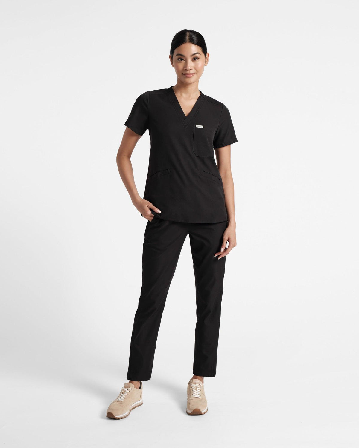 Model in black scrub top with three pockets and matching pants.