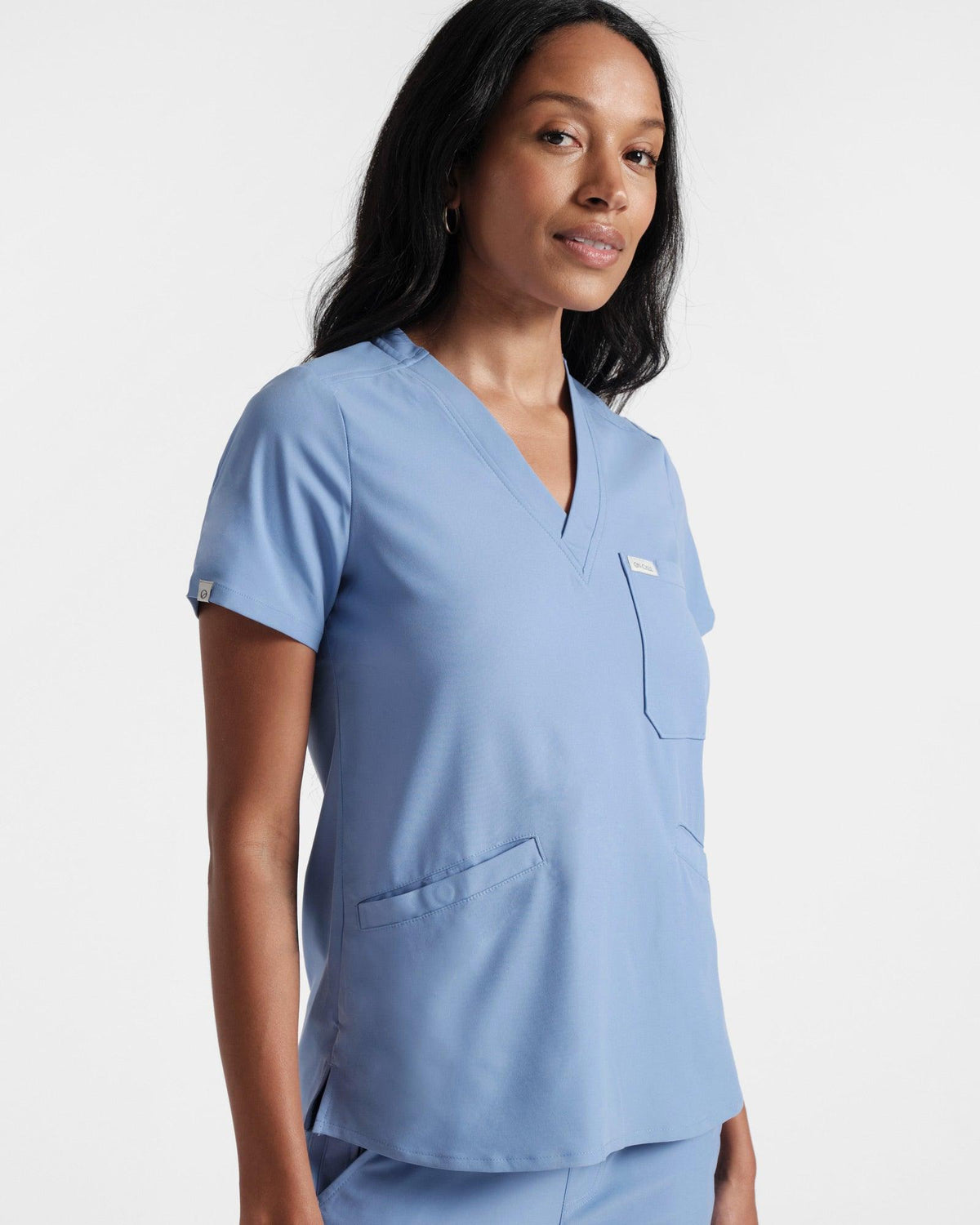 Angled side view of woman in a light blue scrub shirt with a chest pocket and two front pockets.
