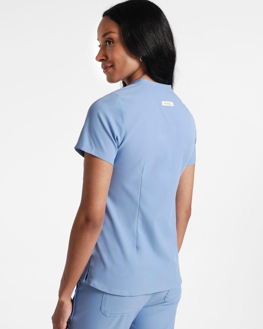 Angled back view of woman in a light blue scrub shirt with dart detailing.