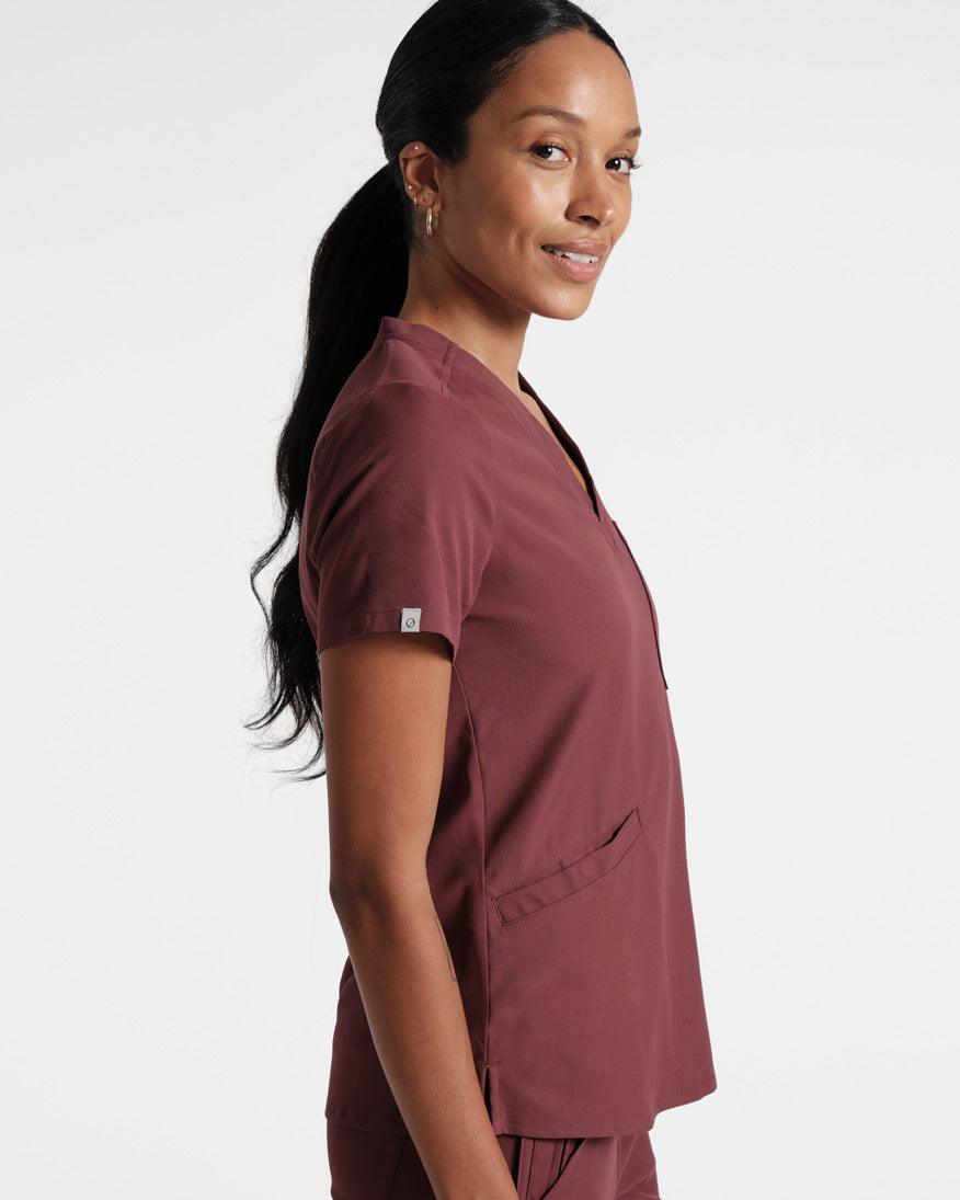 Side view of woman in a deep red scrub shirt with an angled front pocket and small logo fabric label wrapped on the sleeve hem. 