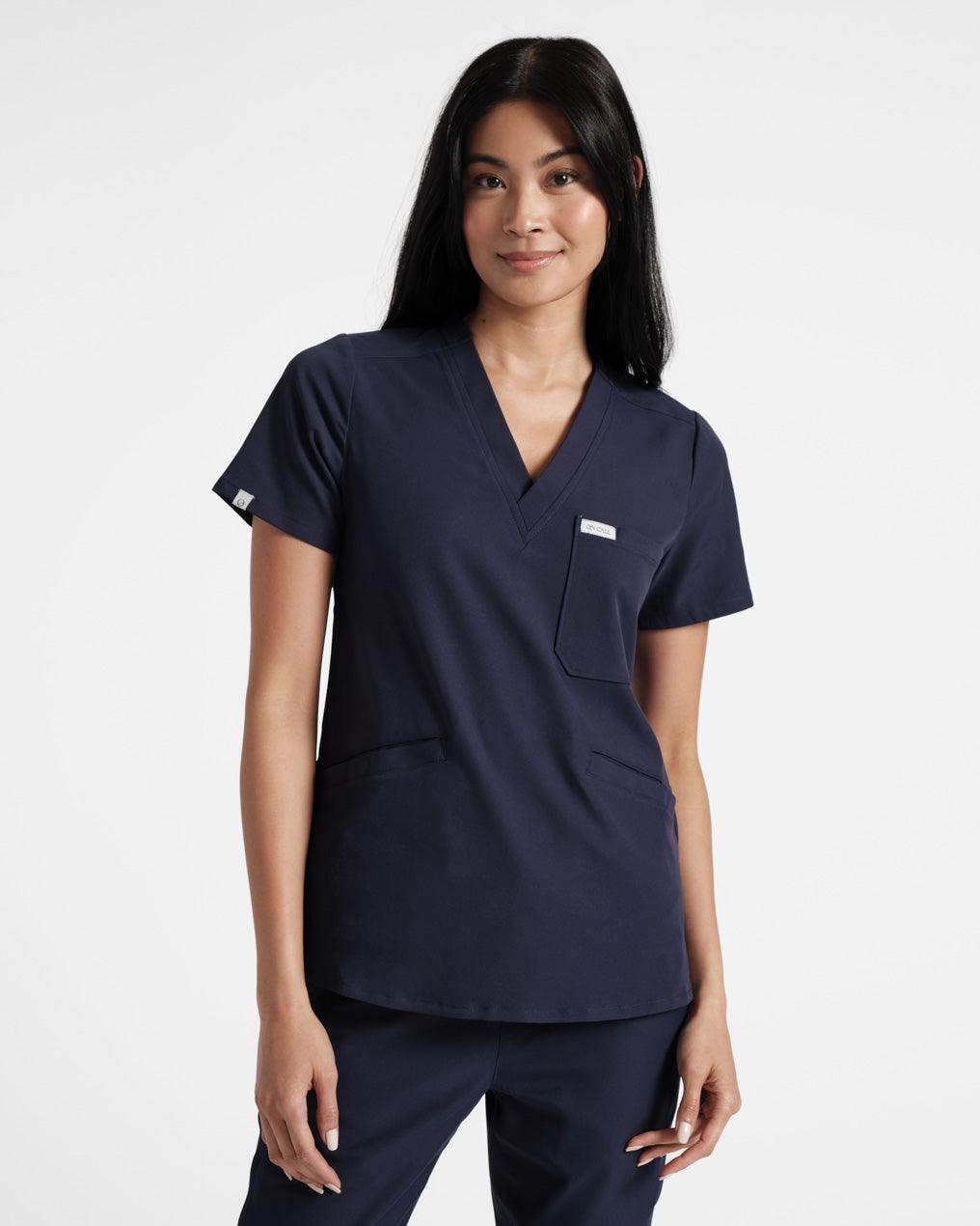 Woman wearing a navy v-neck scrub shirt with a chest pocket and two front pockets.